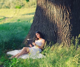 Girl leaning on a tree reading a book Stock Photo