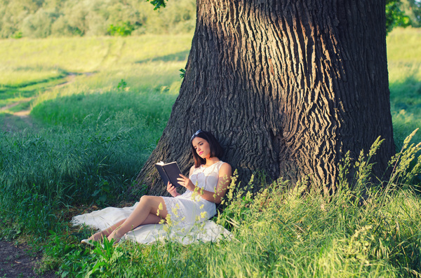 Girl leaning on a tree reading a book Stock Photo