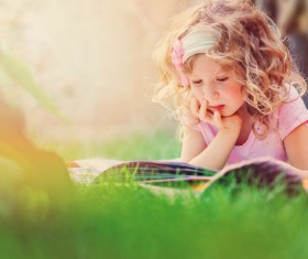 Little girl lying on the grass reading Stock Photo 02