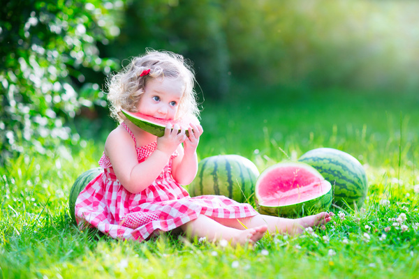 Little girl sitting on the ground eating watermelon Stock Photo