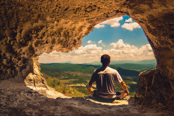 Man sitting in cave mouth meditation Stock Photo