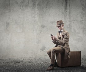 Man sitting on suitcase playing cell phone Stock Photo