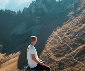 Man sitting on the rock on the mountain and looking at the distant landscape Stock Photo