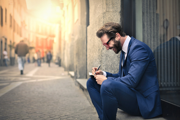 Man sitting on the street recording information smiling Stock Photo