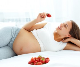 Pregnant woman lying in bed eats strawberries Stock Photo