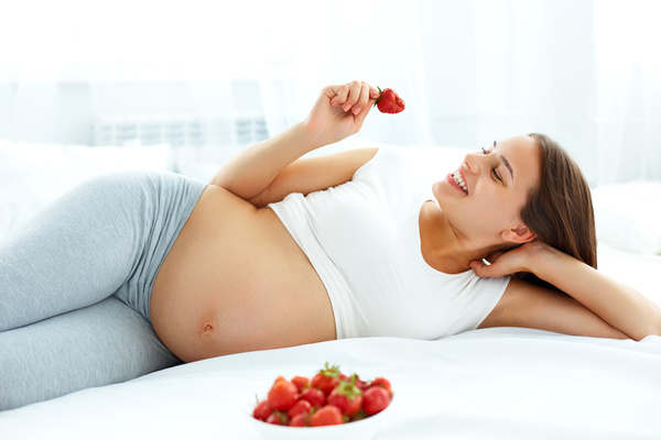 Pregnant woman lying in bed eats strawberries Stock Photo