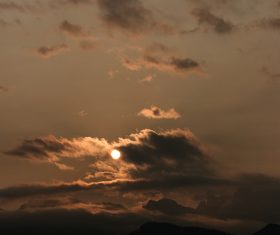 Clouds and sun above mountain range at dusk Stock Photo