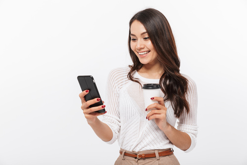 Woman holding coffee looks at mobile phone information Stock Photo