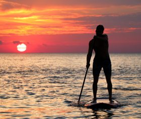 Young man rowing on calm sea at dusk Stock Photo