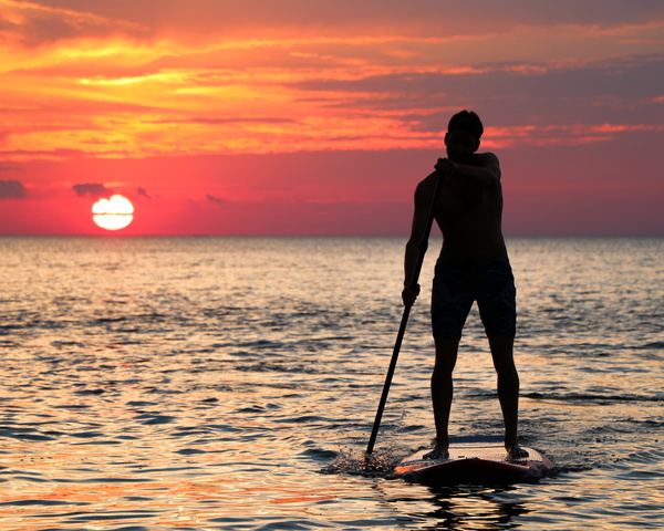 Young man rowing on calm sea at dusk Stock Photo