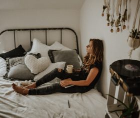 Young woman relaxing with beverage on bed Stock Photo