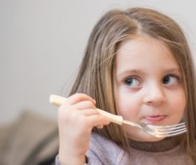 Big eyes little girl eating with a fork Stock Photo