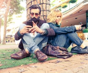Couple sitting under the tree using smartphone Stock Photo