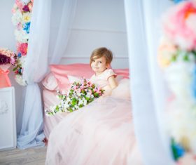 Dressed up beautiful little girl holding bouquet sitting on bed Stock Photo 01