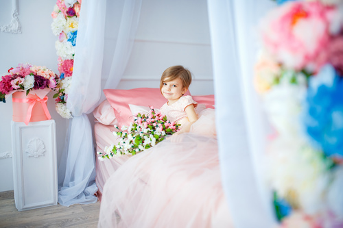 Dressed up beautiful little girl holding bouquet sitting on bed Stock Photo 01