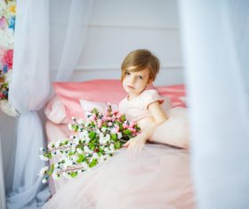 Dressed up beautiful little girl holding bouquet sitting on bed Stock Photo 02