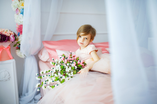 Dressed up beautiful little girl holding bouquet sitting on bed Stock Photo 02