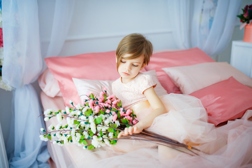 Dressed up beautiful little girl holding bouquet sitting on bed Stock Photo 03