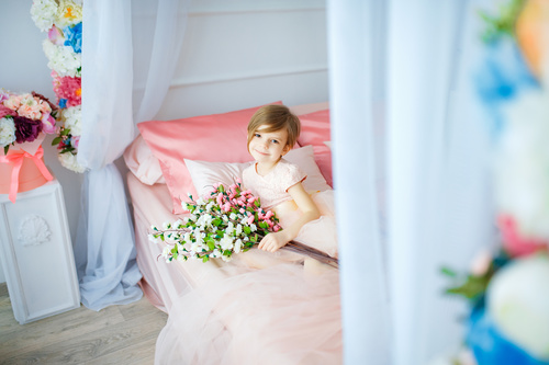 Dressed up beautiful little girl holding bouquet sitting on bed Stock Photo 04