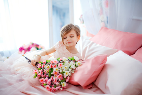 Dressed up beautiful little girl holding bouquet sitting on bed Stock Photo 06
