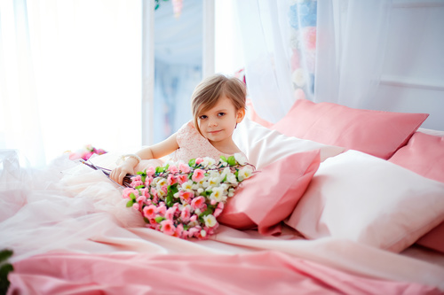 Dressed up beautiful little girl holding bouquet sitting on bed Stock Photo 07