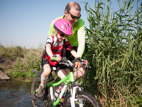 Father pushes bicycle to help children cross the river Stock Photo