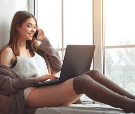 Girl sitting on the window sill and answering the phone Stock Photo