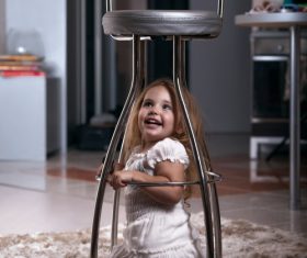 Little girl hiding under metal chair Stock Photo