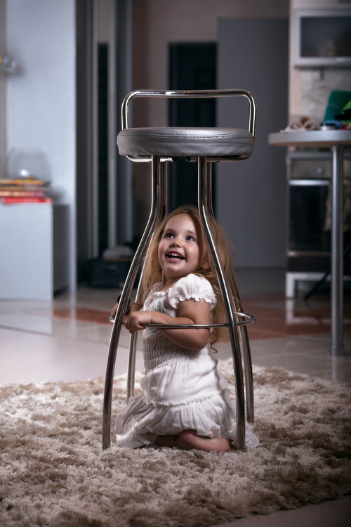 Little girl hiding under metal chair Stock Photo