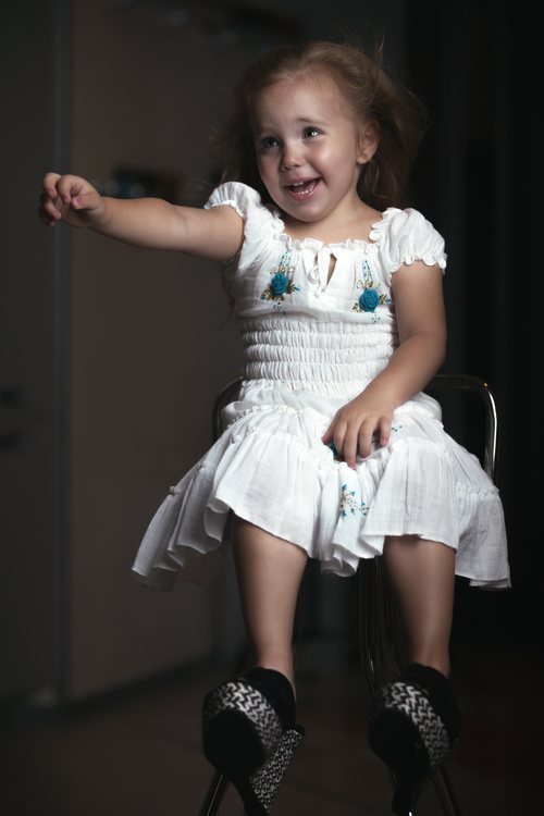 Little girl wearing moms high heels sitting on metal chair Stock Photo 01