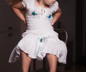 Little girl wearing moms high heels sitting on metal chair Stock Photo 02