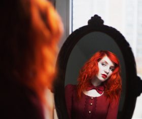 Redhead girl looks in the mirror Stock Photo