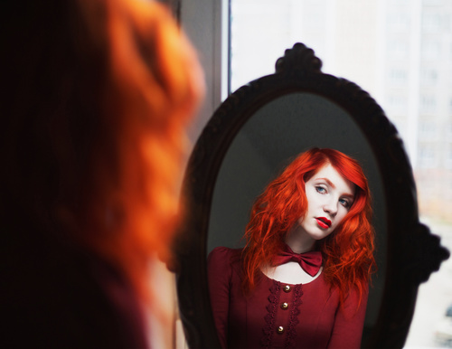 Redhead girl looks in the mirror Stock Photo