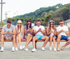 Young people sitting on bench and playing with smartphone Stock Photo