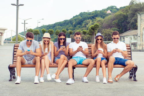 Young people sitting on bench and playing with smartphone Stock Photo
