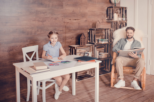 Father reading book and daughter doing homework Stock Photo