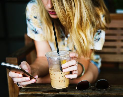 Girl holding drink and playing with mobile phone Stock Photo