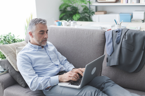 Man leaning on the couch using laptop Stock Photo