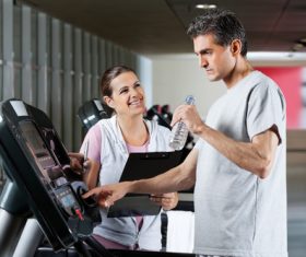 Smiling female coach guiding elderly man to exercise on treadmill Stock Photo