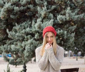 Woman in knit sweater standing in front of pine tree Stock Photo 01