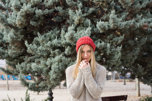 Woman in knit sweater standing in front of pine tree Stock Photo 01