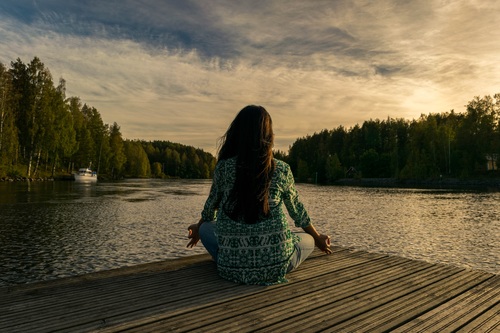 Woman sitting facing the lake cross-legged Stock Photo