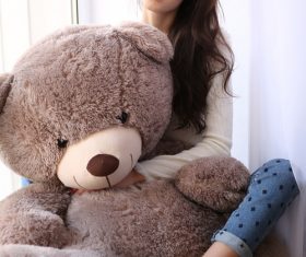 Woman sitting on the window sill holds big teddy bear Stock Photo