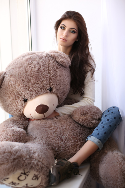 Woman sitting on the window sill holds big teddy bear Stock Photo