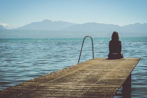 Woman sitting on wooden pier looking at the sea Stock Photo