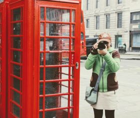 Woman taking photos with camera at red phone booth Stock Photo