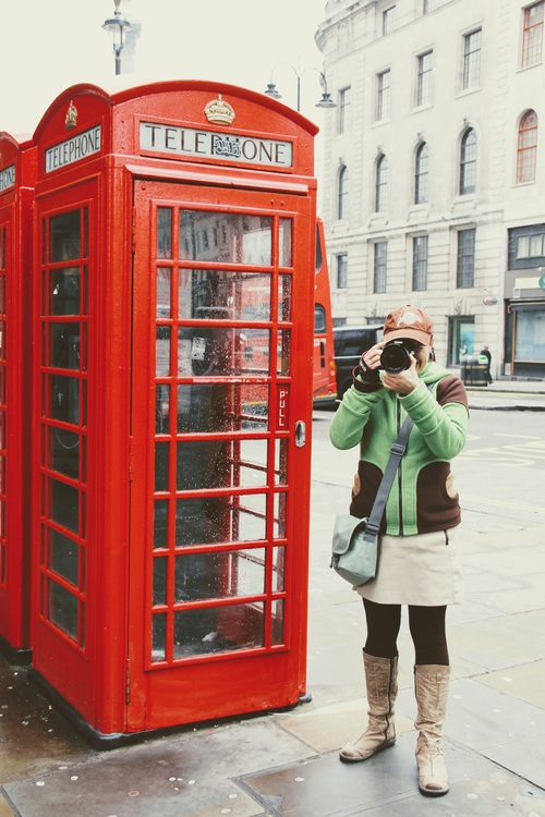 Woman taking photos with camera at red phone booth Stock Photo