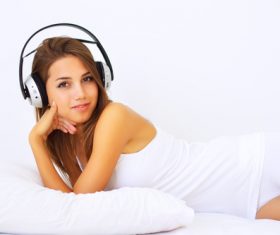 Young girl lying in bed wearing headphones Stock Photo