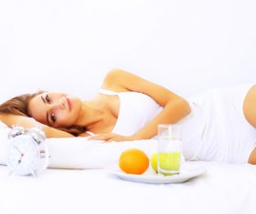 Young girl lying on the bed and putting fruit plate next to it Stock Photo