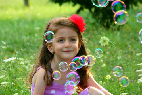 Little girl sitting on the grass looking at soap bubbles Stock Photo